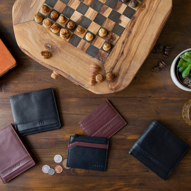 Men's various leather wallets in brown and black on a coffee table with a chessboard.