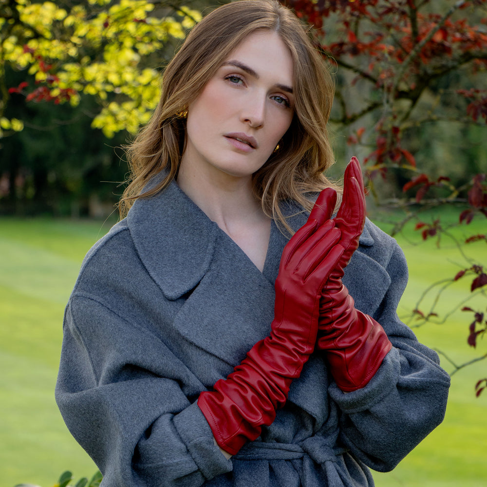 Woman wearing long red leather gloves and a grey coat in the countryside