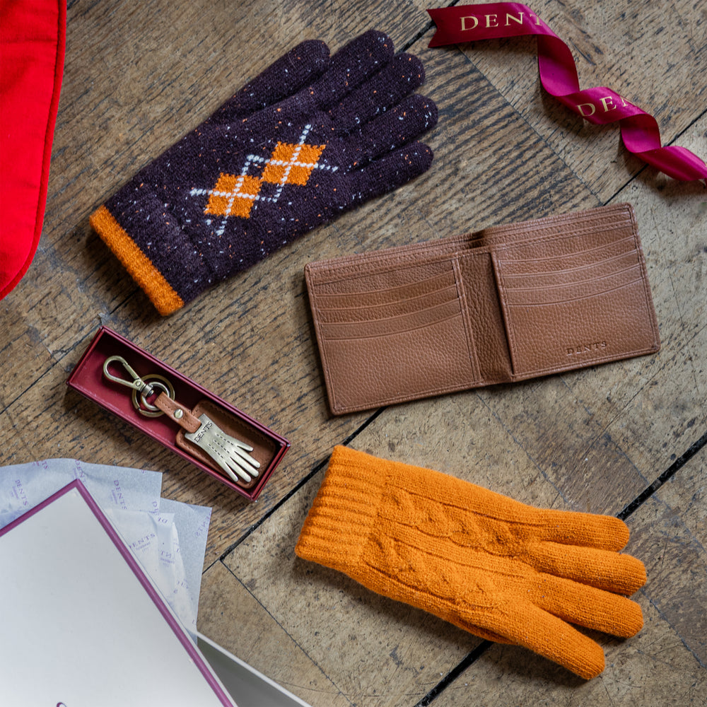 Christmas stocking fillers including knitted gloves for men and women, a men's leather wallet and keyring against a festive background