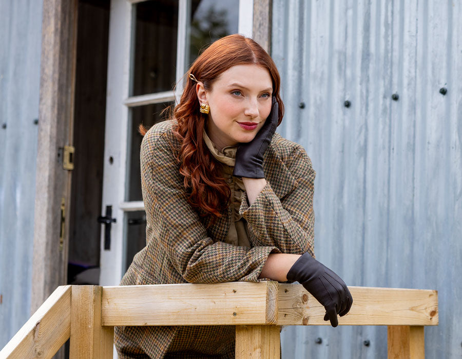 Woman wearing cashmere-lined leather gloves leaning on a wooder banister outside a cabin