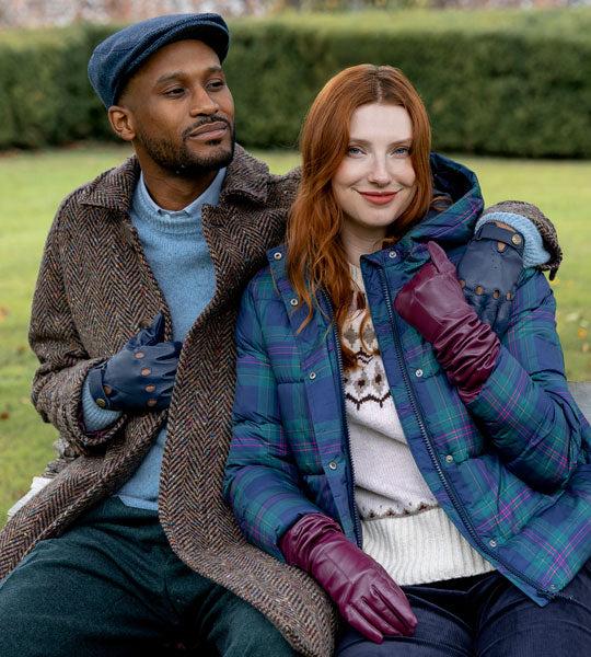 Man and woman sitting outdoors on a bench wearing leather gloves and tweed hat