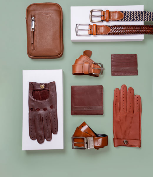Men's leather gifts including bags, belts, gloves and wallets in various colours and styles on a green background