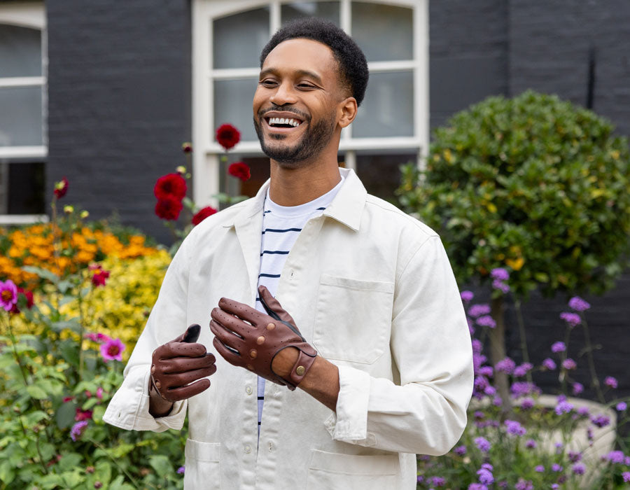Man wearing touchscreen leather driving gloves in tan and black, outside in the garden. 