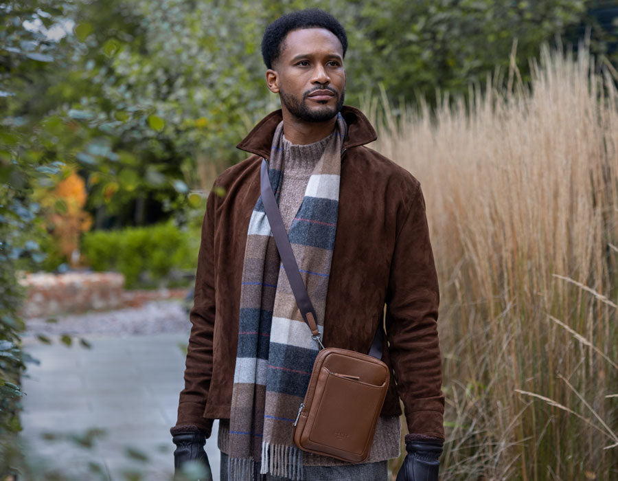 Man wearing a plaid cashmere scarf and holding a brown crossbody bag, standing outdoors.