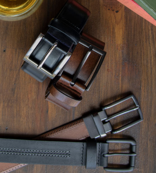 Four leather belts with metal buckles on a wooden surface.